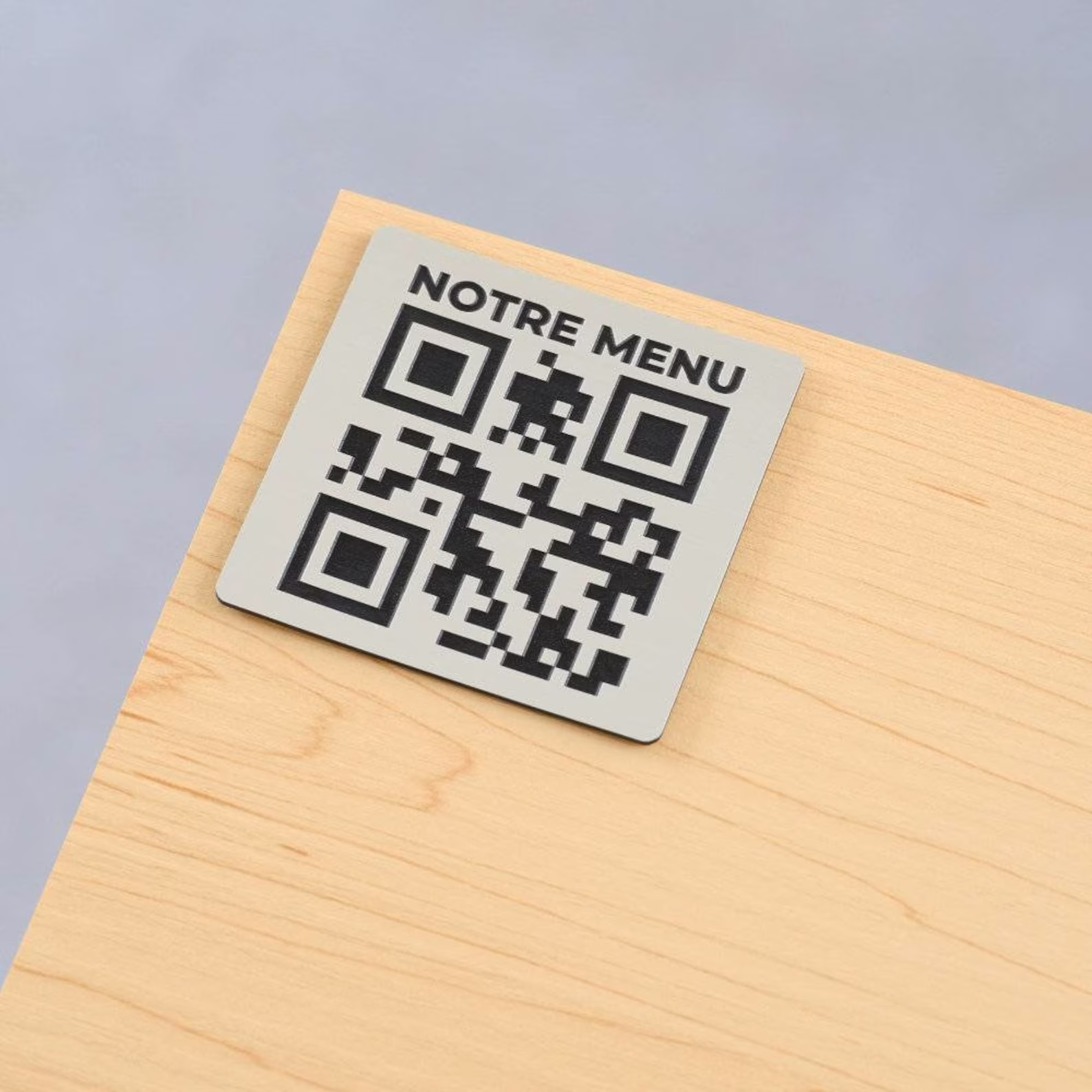 Kovový gravírovaný QR kód s nápisom Notre Menu na rohu stola