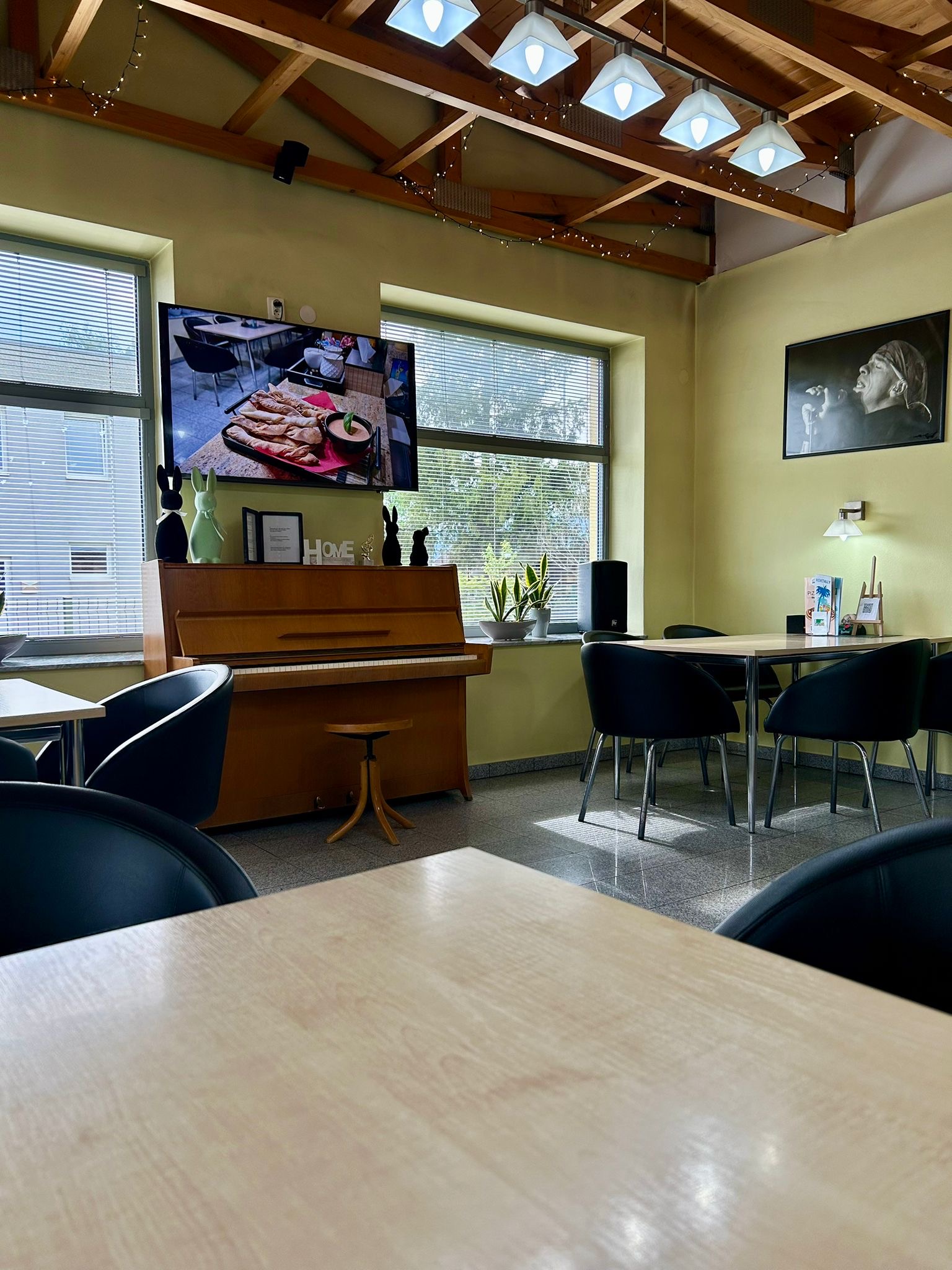 Smart TV showing digital restaurant menu board above a piano in a cozy dining space