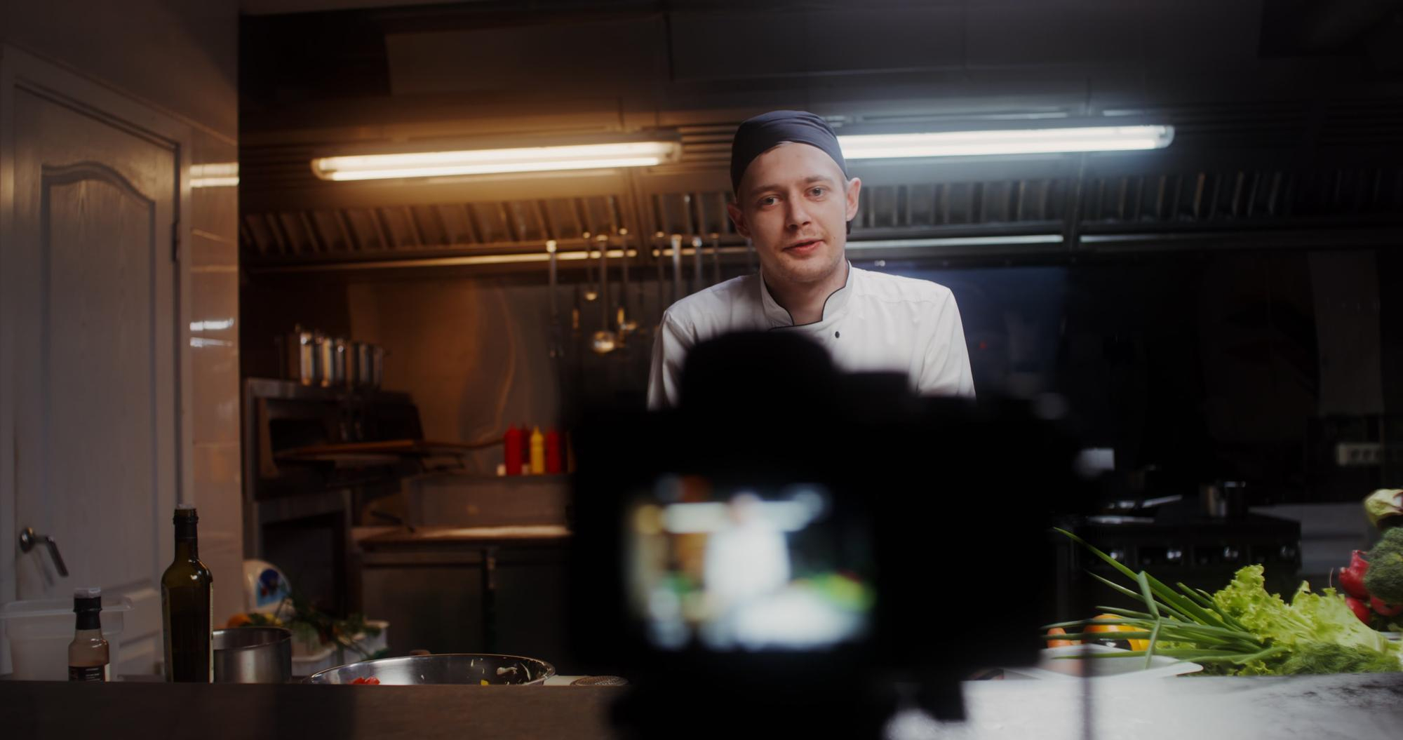 A chef in a professional kitchen, looking directly at the camera, suggesting a video for Facebook Posts Ideas for Restaurants, showcasing behind-the-scenes content.